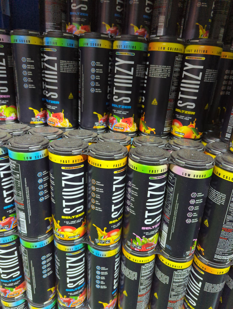 Stiizy seltzer cans in black packaging with colorful fruit graphics, stacked on store shelves, labeled as low sugar and fast acting.